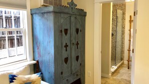 A room with a blue cabinet with heart and cross cutouts, a white couch with patterned pillows, and a bathroom with a stone wall and bamboo ladder.