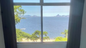 Una habitación con una cama, un ventanal con vistas a la playa y al mar, y cortinas.