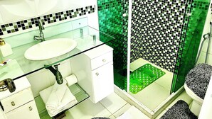 Un baño con lavamanos de vidrio, armarios blancos, cabina de ducha verde y pared de ducha con diseño a cuadros blanco y negro.