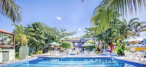A pool area with clear blue water, surrounded by palm trees and umbrellas. - Pousada Recanto Shangri-lá (Cabo Frio)
