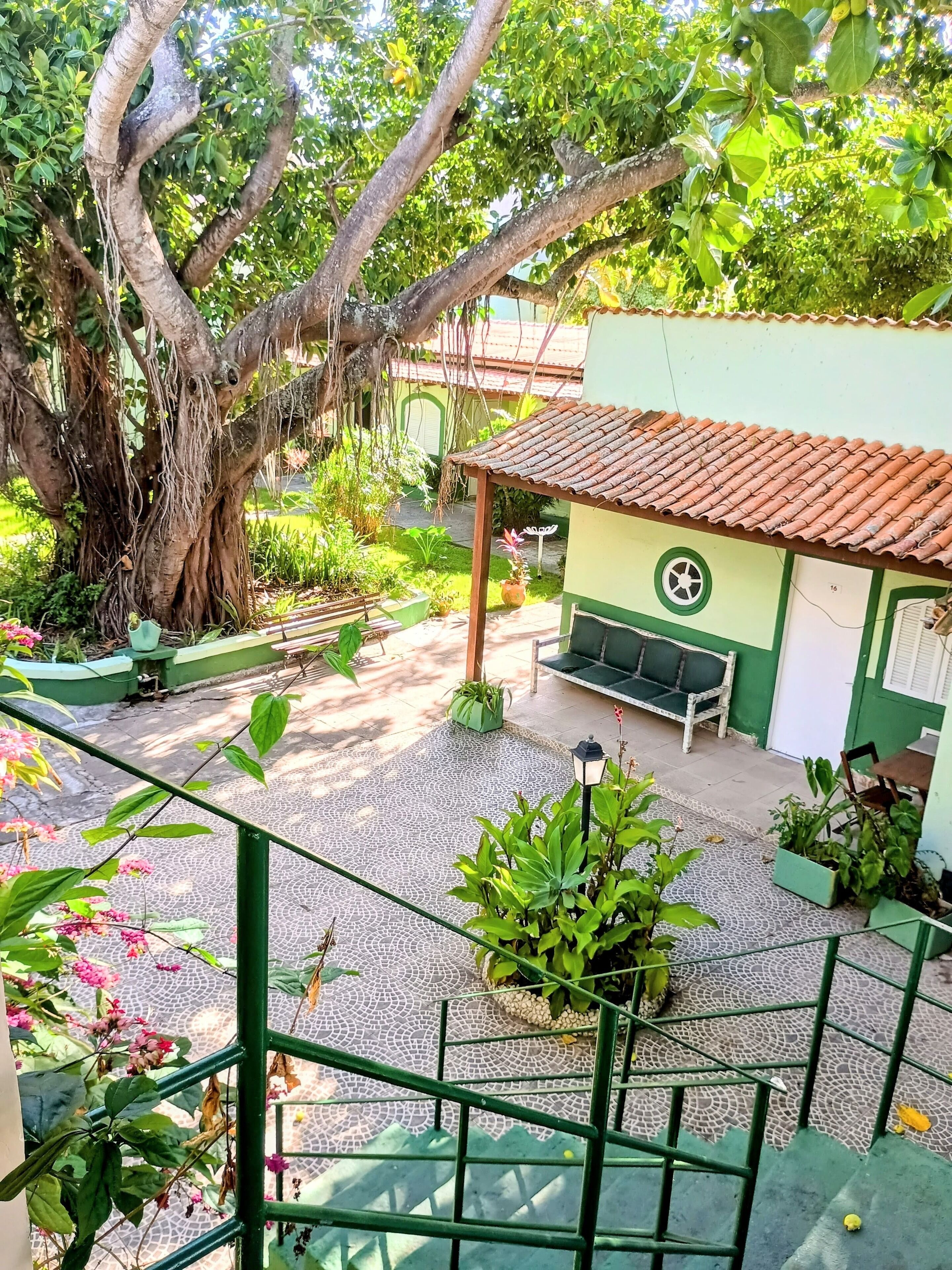 Um pátio com uma árvore grande, uma área de estar coberta e piso de azulejos.