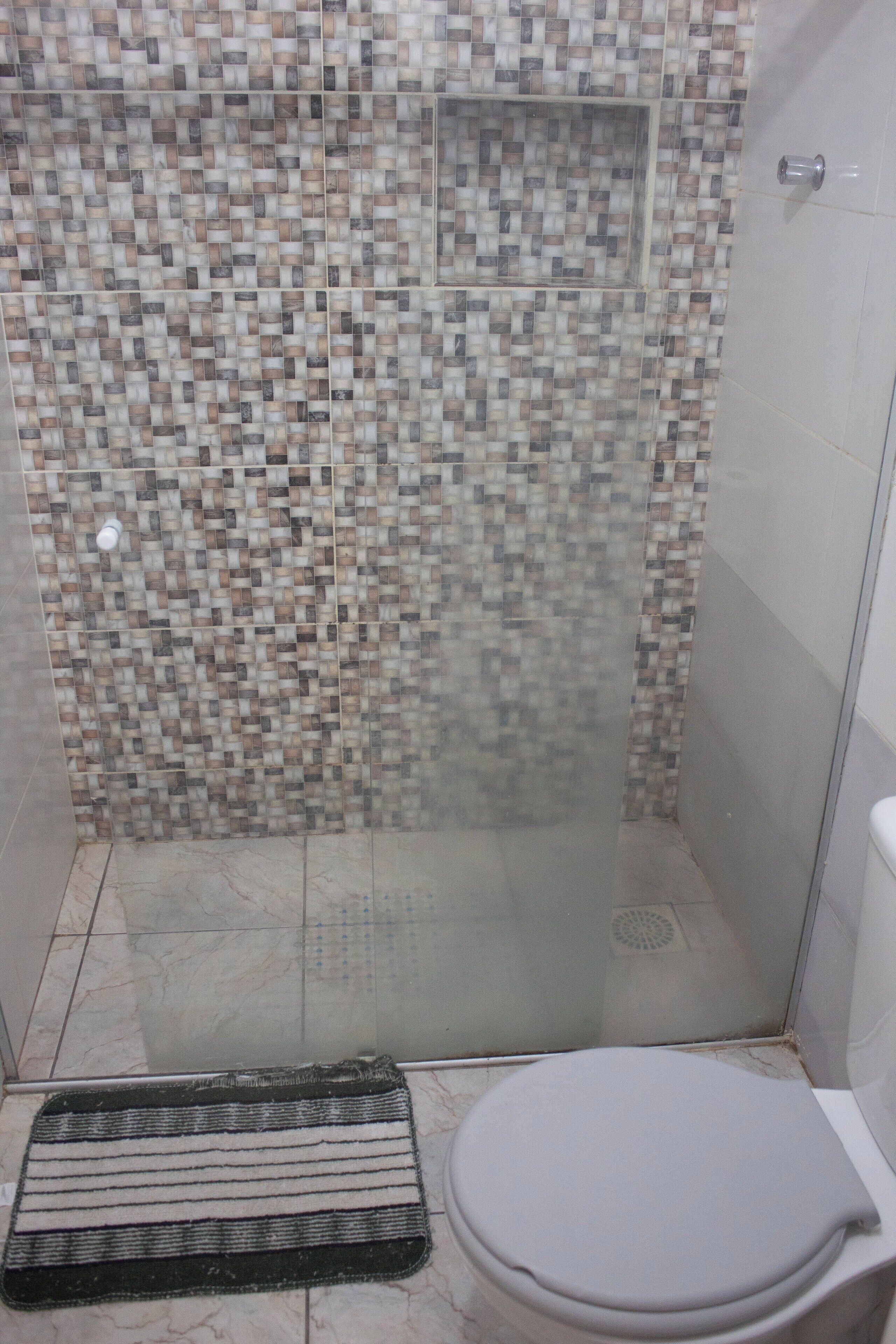 Een douche met een betegelde wand en een glazen deur.