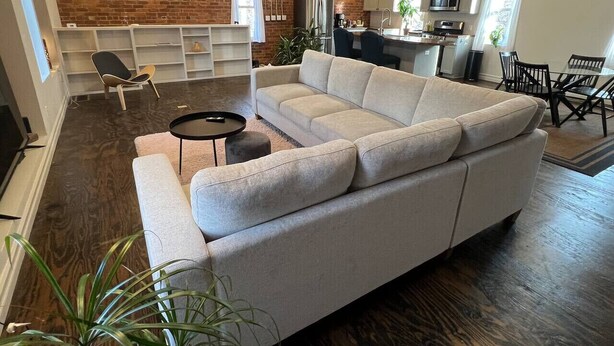 A modern living room with a sectional sofa, a small round table, and a brick accent wall.