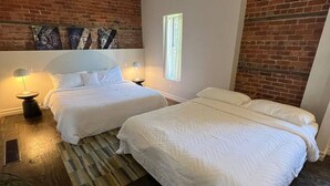 A bedroom with two beds, a brick wall, and a window.