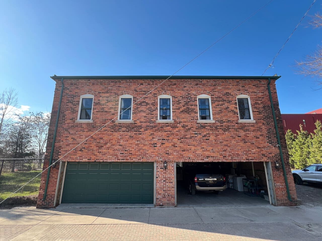 A two-story brick building with a green garage door, a covered driveway, and a parked car inside.