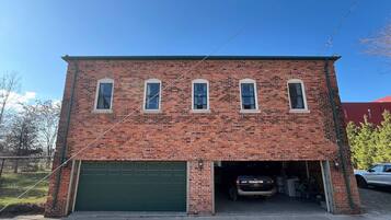 A two-story brick building with a green garage door, a covered driveway, and a parked car inside.