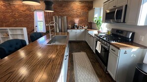 A modern kitchen with a wooden island, stainless steel appliances, and a brick wall.