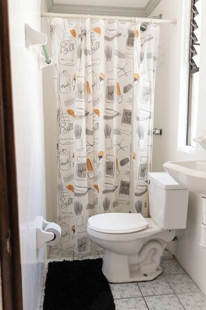 Enjoy a refreshing shower in this bathroom with a shower curtain featuring a playful pattern, a white toilet, and a black rug.
