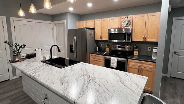 A modern kitchen with a marble island, wooden cabinets, stainless steel appliances, and pendant lighting.
