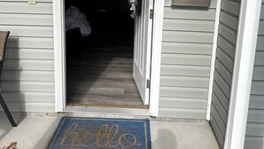 A house entrance with a white door, a blue mat with "hello" on it, and a small porch area.