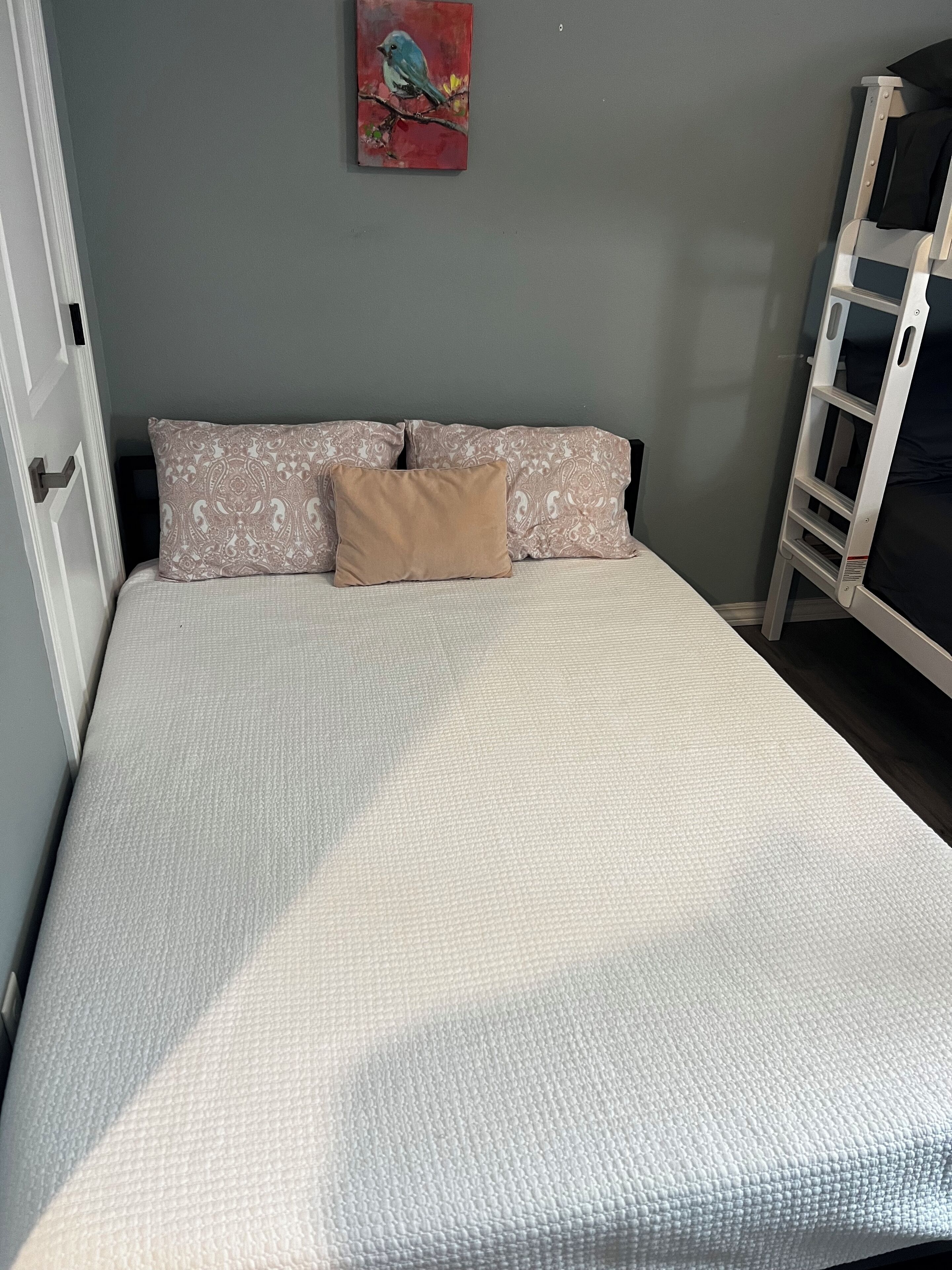 A bedroom with a bed, patterned pillows, a wall painting, and a white ladder.