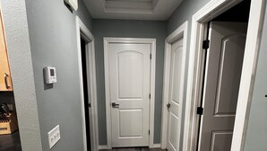 A hallway with a white door at the end, a light fixture on the ceiling, and a light switch on the wall.