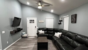 A modern living room with a black leather couch, a wooden coffee table, and a ceiling fan.