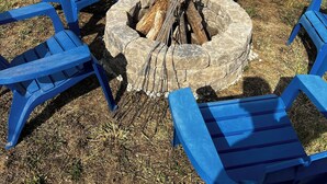 A backyard with a fire pit surrounded by blue Adirondack chairs.