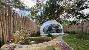 A garden with a stone fountain, a white geodesic dome structure, and a bamboo fence. - Glamping Lake San Juan (San Juan de la Maguana)