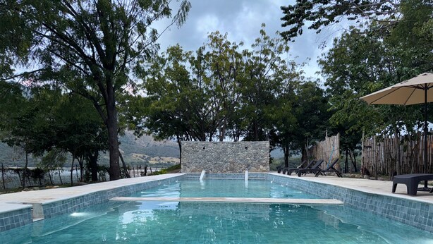 A swimming pool with tiled edges, surrounded by trees and a stone wall. - Glamping Lake San Juan (San Juan de la Maguana)