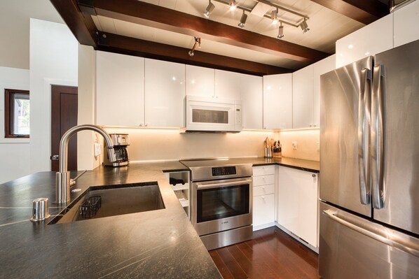 Una cocina moderna con electrodomésticos de acero inoxidable, horno empotrado, microondas y refrigerador, y una encimera oscura.