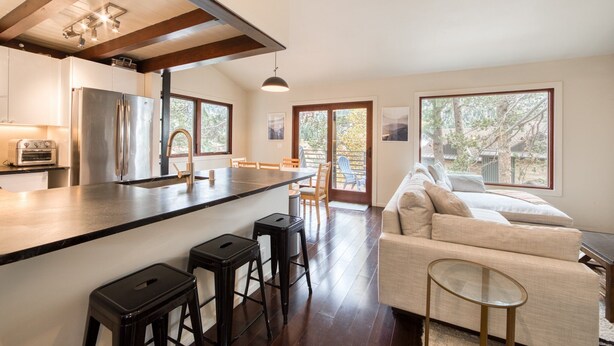 Una cocina moderna con una isla central, taburetes de bar y un comedor con sofá y sillas.