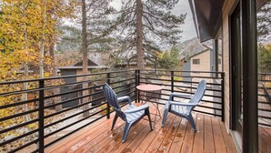 Una terraza de madera con dos sillas y una mesita, con vistas a una zona residencial con casas y árboles.