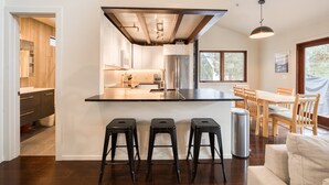 Una cocina moderna con una isla central, taburetes de bar y un comedor con sillas de madera y una mesa.