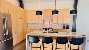 Una cucina moderna con mobili in legno, un frigorifero in acciaio inossidabile, un'isola centrale con sgabelli da bar e illuminazione a sospensione.