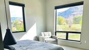 Una camera da letto con un letto, una sedia, una scrivania e ampie finestre che si affacciano su un paesaggio.