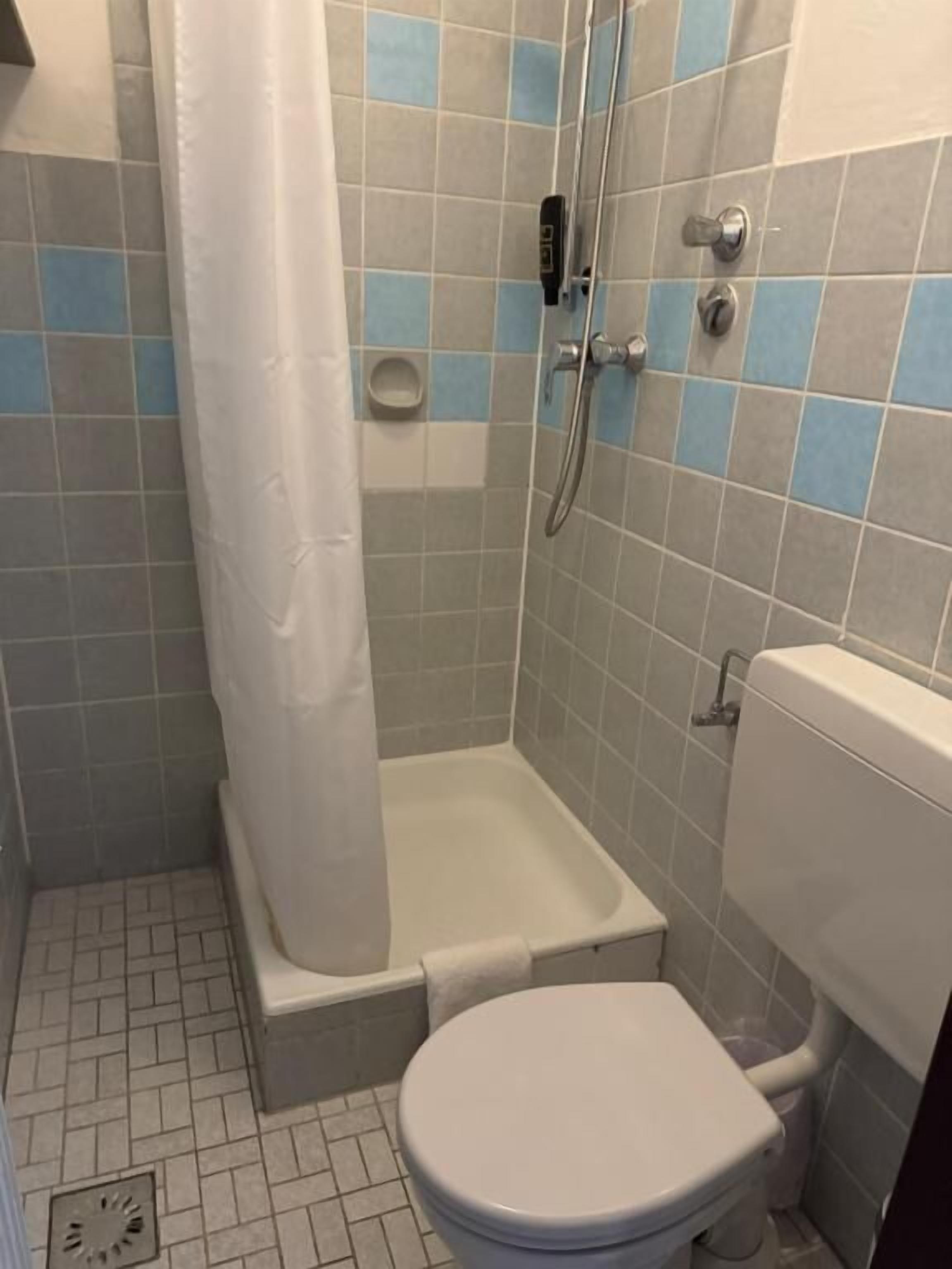 Un baño con ducha, inodoro y un lavamanos pequeño.