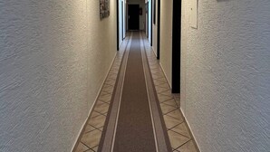 A long, narrow hallway with a patterned carpet, white walls, and a cityscape painting on the right.