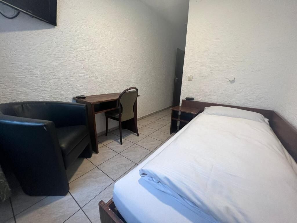A small, simple room with a bed, a desk, and a chair.