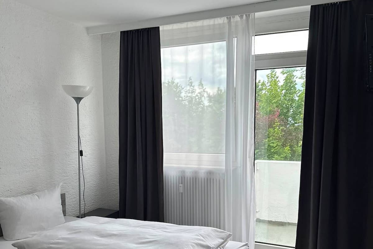 A hotel room with a bed, a chair, a floor lamp, and a view of trees through a window.