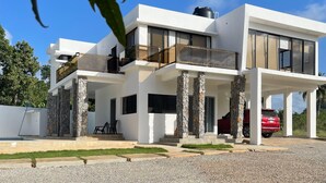 Une maison moderne à deux étages, dotée d’une façade en pierre, de grandes fenêtres et d’une voiture rouge garée dans l’allée.