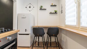 Eine moderne Küche mit Kühlschrank, zwei Barhocker, einer Holz Arbeitsplatte und einer Wanduhr.