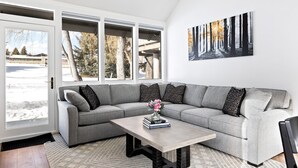 A modern living room with a grey sectional sofa, a coffee table, and a large window with a view of a snowy landscape. - Payday at Park City, Luxury Renovated Townhome, Walk to Silver Star Lift, New Bullfrog Spa (Park City)