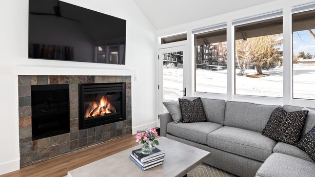 A modern living room with a stone fireplace, a grey sofa, and a coffee table with books and flowers. - Payday at Park City, Luxury Renovated Townhome, Walk to Silver Star Lift, New Bullfrog Spa (Park City)