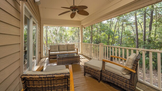 A covered porch with wicker furniture, a ceiling fan, and a view of a forest.
