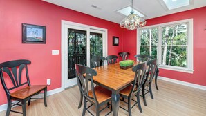 A dining room with a wooden table and chairs, red walls, and a view through large windows.
