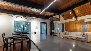 Ampla sala de estar com uma grande mesa de jantar, um sofá e teto de madeira.