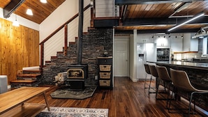 Cozinha moderna com lareira de pedra, piso de madeira e área de bar com banquetas.