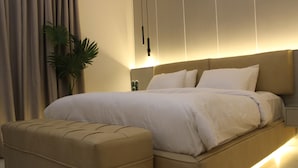 Une chambre à coucher moderne avec un grand lit, un pouf assorti, une table de chevet et une plante en pot.