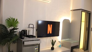 Une chambre d’hôtel moderne équipée d’un téléviseur à écran plat fixé au mur, d’un bureau avec une machine à café, d’une petite plante en pot et d’un meuble-miroir.