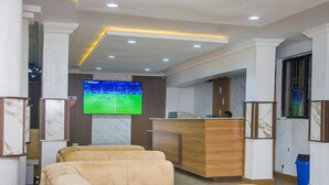 Un vestíbulo de hotel con una recepción, un televisor montado en la pared y dos sofás cómodos.