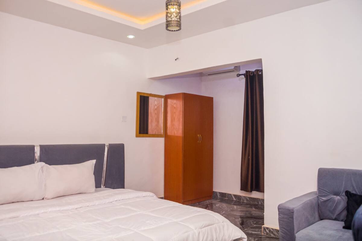 A hotel room with a bed, a wardrobe, a chair, and a shower area.