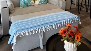 Un salon comprenant un canapé, une table basse ornée d’un chemin de table à rayures bleues et blanches, et un vase contenant des fleurs orange.