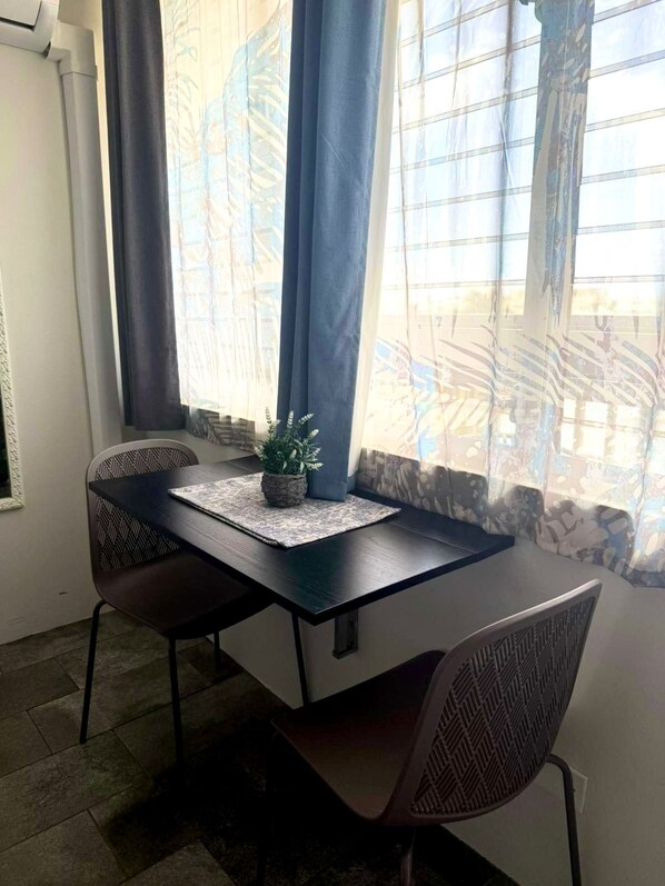 Un comedor con una mesa, sillas, una planta en maceta y un ventanal con cortinas.