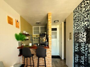 Una cocina con barra, dos sillas, una planta en maceta y un panel decorativo en la pared.