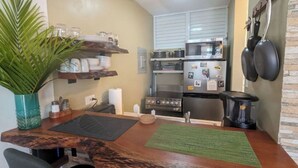 Une cuisine compacte avec un plan de travail en bois, deux chaises, une petite plante en pot et un four à micro-ondes placé au-dessus de la cuisinière.