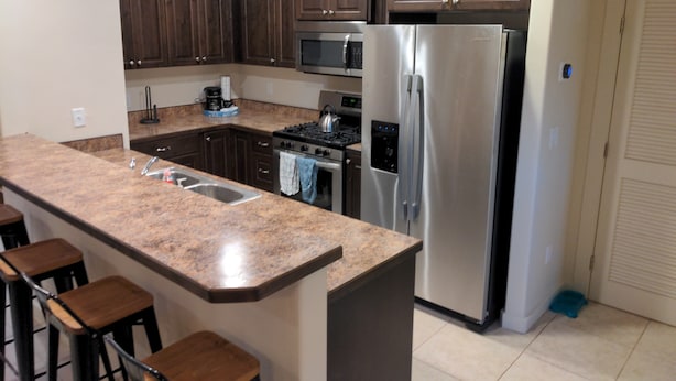 A modern kitchen with dark wood cabinets, a stainless steel refrigerator, a gas stove, and a granite countertop.