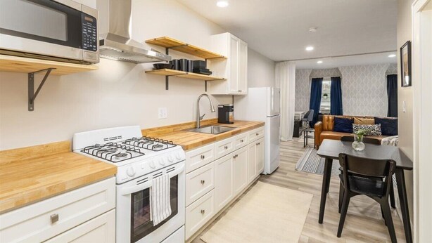 A modern kitchen with white cabinets, a gas stove, a microwave, and wooden shelves. - Cozy Studio Near Children’s Hospital, Kitchen & Laundry (Columbus)
