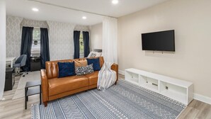 A modern living room with a leather sofa, a TV mounted on the wall, and a patterned rug. - Cozy Studio Near Children’s Hospital, Kitchen & Laundry (Columbus)