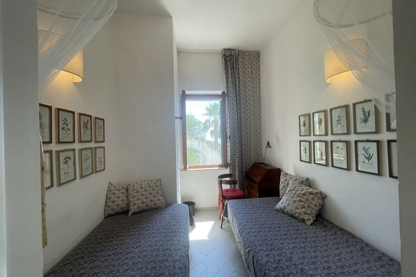 Een kamer met twee bedden, een raam en kunstwerken in lijsten aan de muren.